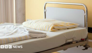 Generic stock image of a hospital / care home bed, it has yellow folded sheets matching the wall behind it