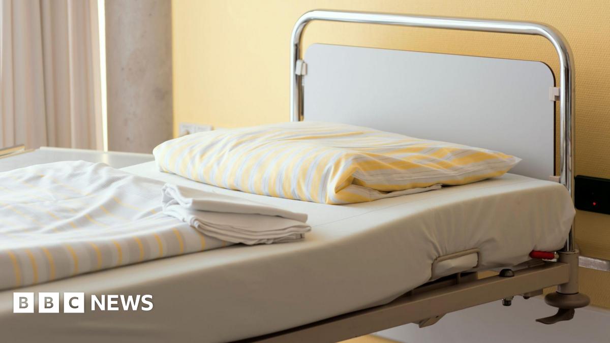 Generic stock image of a hospital / care home bed, it has yellow folded sheets matching the wall behind it