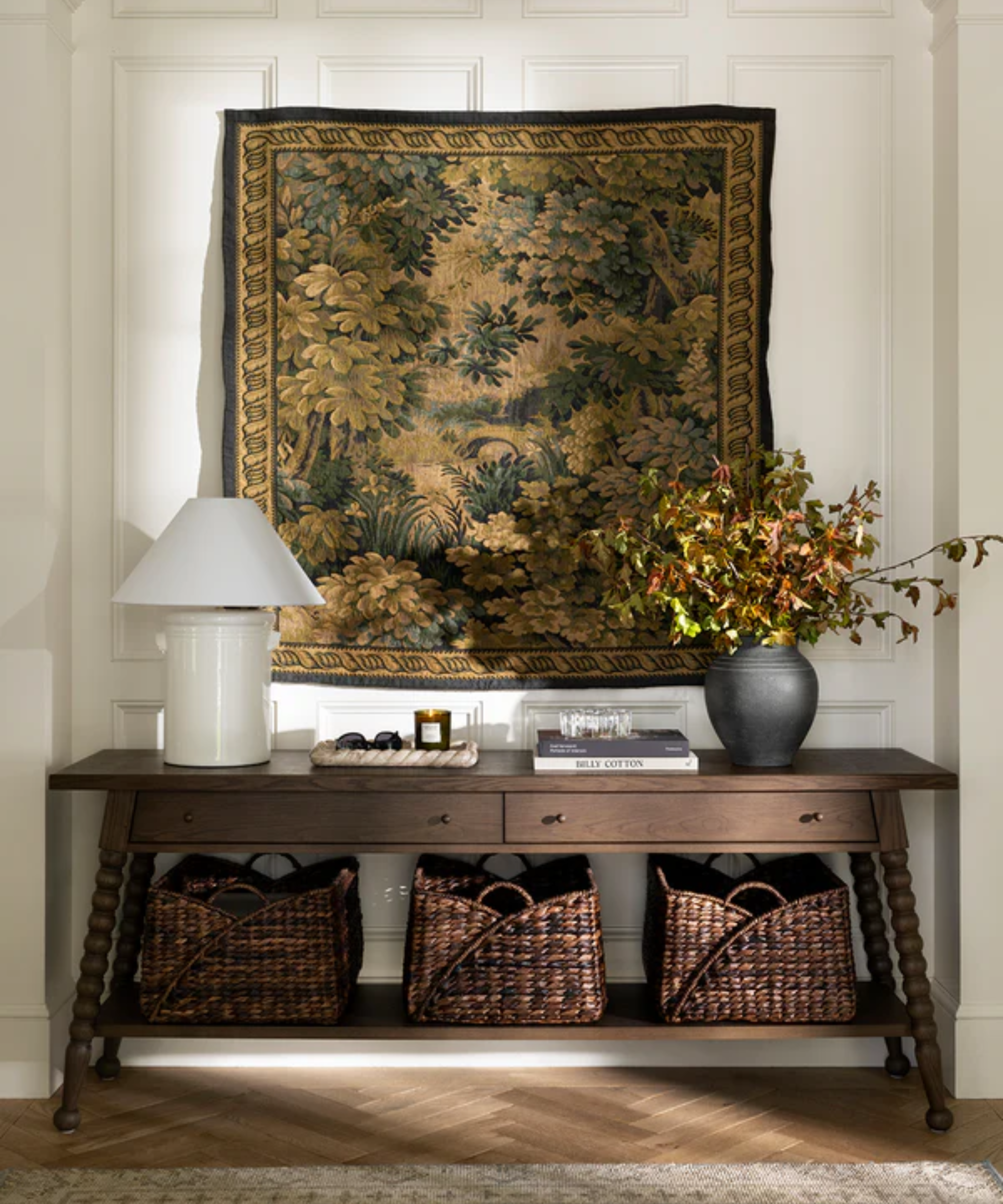 dark wood credenza with decor on top, three dark woven baskets below, and a tapestry hanging from the wall above