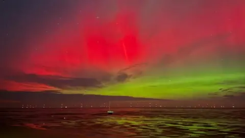 Natalie Cherubini Vivid pink, red and green lights are visible in the night sky above the sea