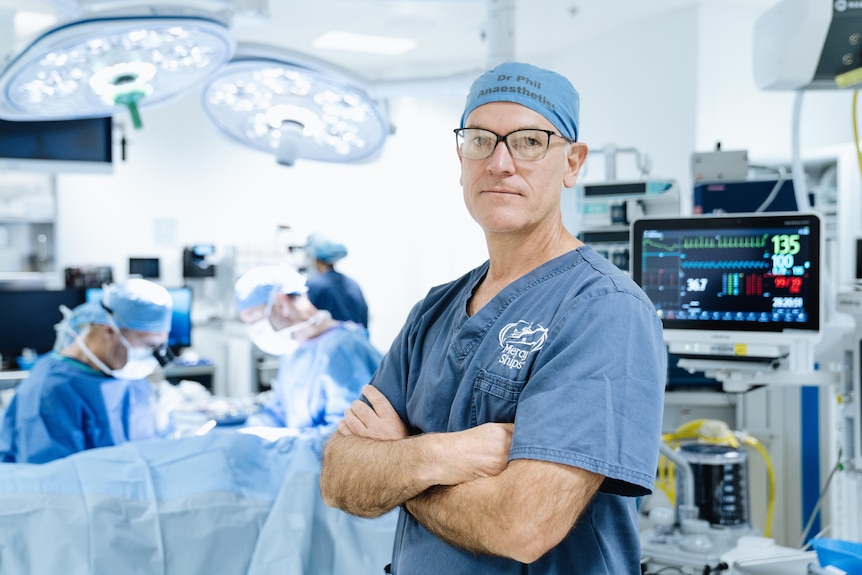 a man in scrubs looks at the camera, behind him is an operating theatre