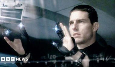 Scene from the film Minority Report. A man (the actor Tom Cruise in the film Minority Report) stares at a transparent screen, wearing black gloves with bright lights on them.
