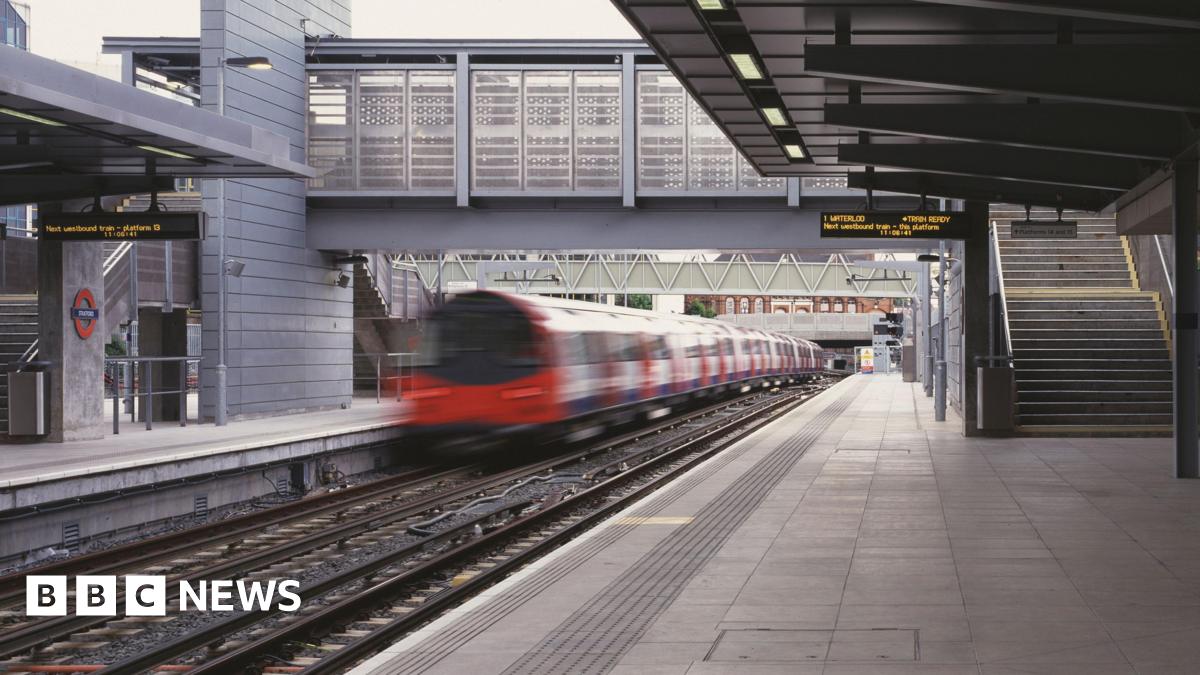 Platform at Stratford station shows departing Jubilee line train on left with bridge ahead and steps to the right. A departure board shows Waterloo