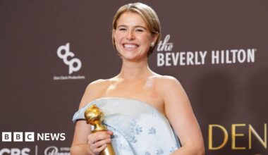 A close-up of Jessie Buckley attending the 2026 BAFTA Tea Party in Los Angeles.  She has short, wavy blonde hair and is pictured in front of a purple background.