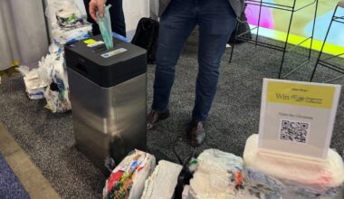 The bottom half of a man dropping a plastic bag in a machine, the Soft Plastic Compressor, that is ingesting plastic bags.