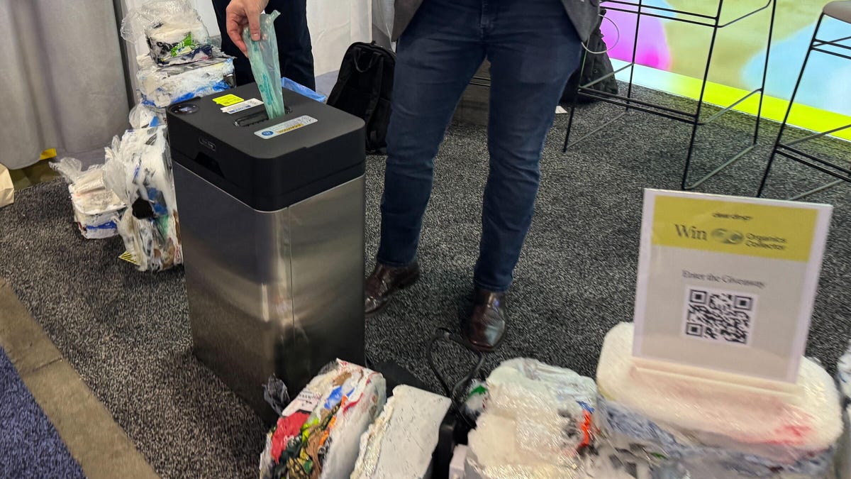 The bottom half of a man dropping a plastic bag in a machine, the Soft Plastic Compressor, that is ingesting plastic bags.