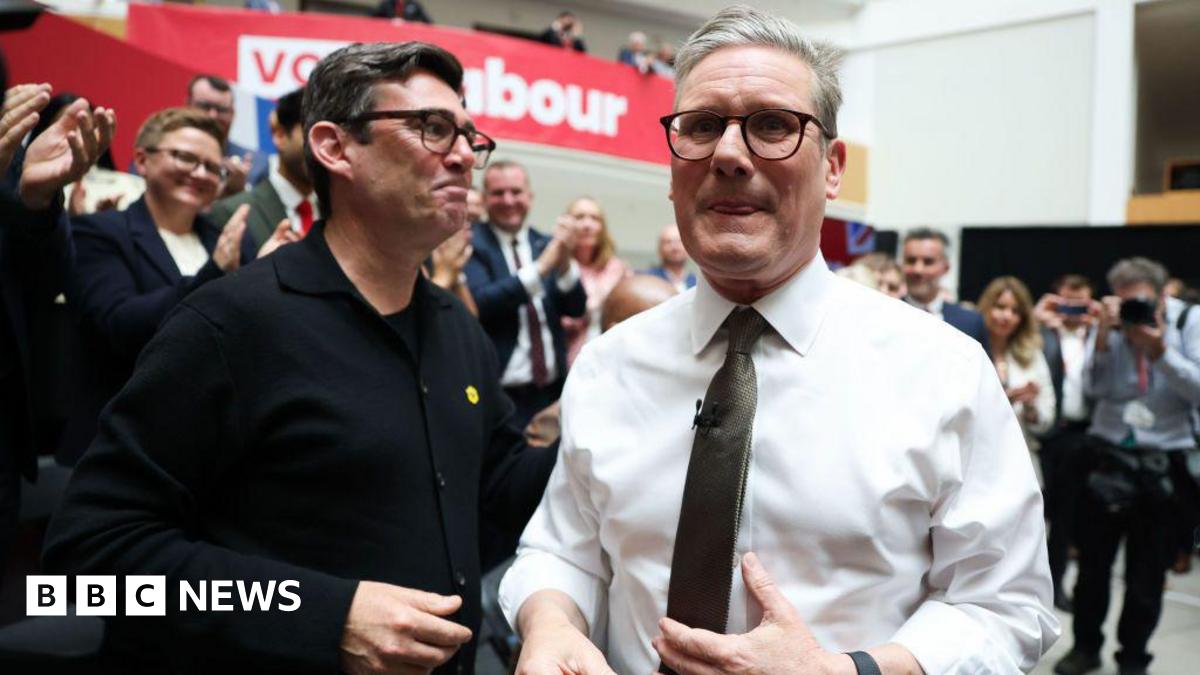 Starmer and Burnham pictured together at the launch of the Labour manifesto in 2024, surrounded by an applauding crowd.