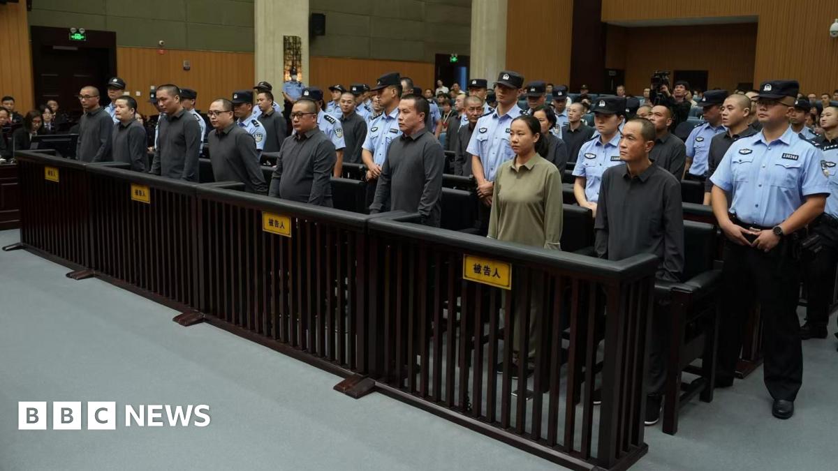People stand in a row in a court, surrounded by security officers