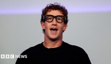 Meta CEO Mark Zuckerberg speaking on stage in a simple black t-shirt wearing thick rimmed black eye glasses, a prototype of an in-development wearable product.