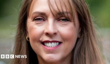 Donald Trump and Keir Starmer sit in a formal drawing room setting  on arm chairs with US and UK  flags behind them. Both have serious expressions and are looking out and not at each other.