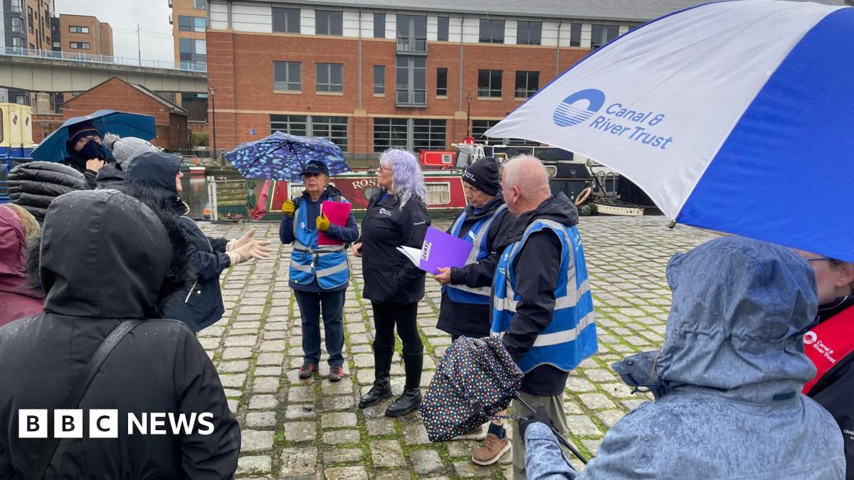 Four volunteers leading a history walk at Victoria Quays surrounded by people with jackets on and hoods up because it's raining