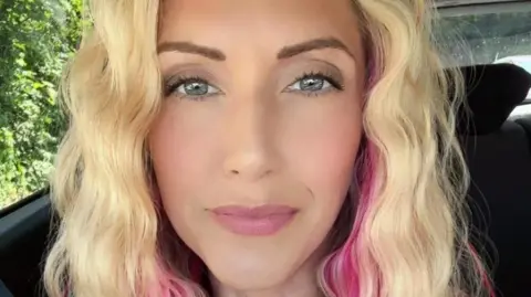 Jessica Mason Jessica, who has curly blonde hair and pink highlights, with blue eyes, smiles as she sits in a car