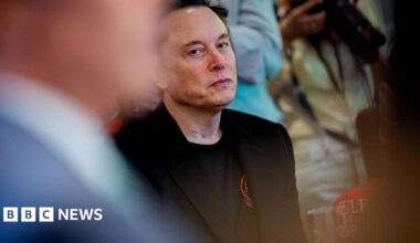 Donald Trump and Keir Starmer sit in a formal drawing room setting  on arm chairs with US and UK  flags behind them. Both have serious expressions and are looking out and not at each other.