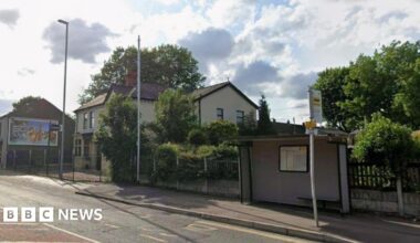 Carters Arms on Manchester Old Road Middleton is obscured by trees, a lampost and phone mast. There is a buys shelter and stop to its left.
