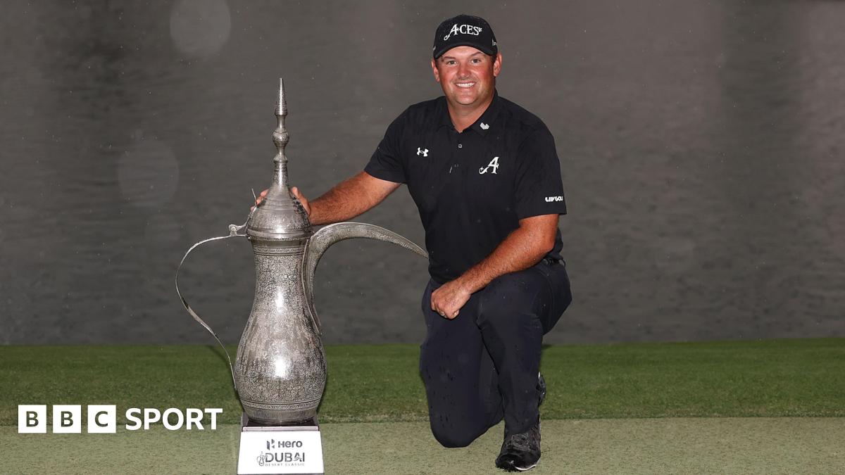 Patrick Reed, dressed in black, kneels down beside the Desert Classic trophy