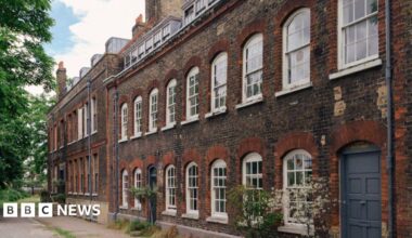 Exterior of brick building shows nine white sash windows upstairs and another seven downstairs plus a grey front door
