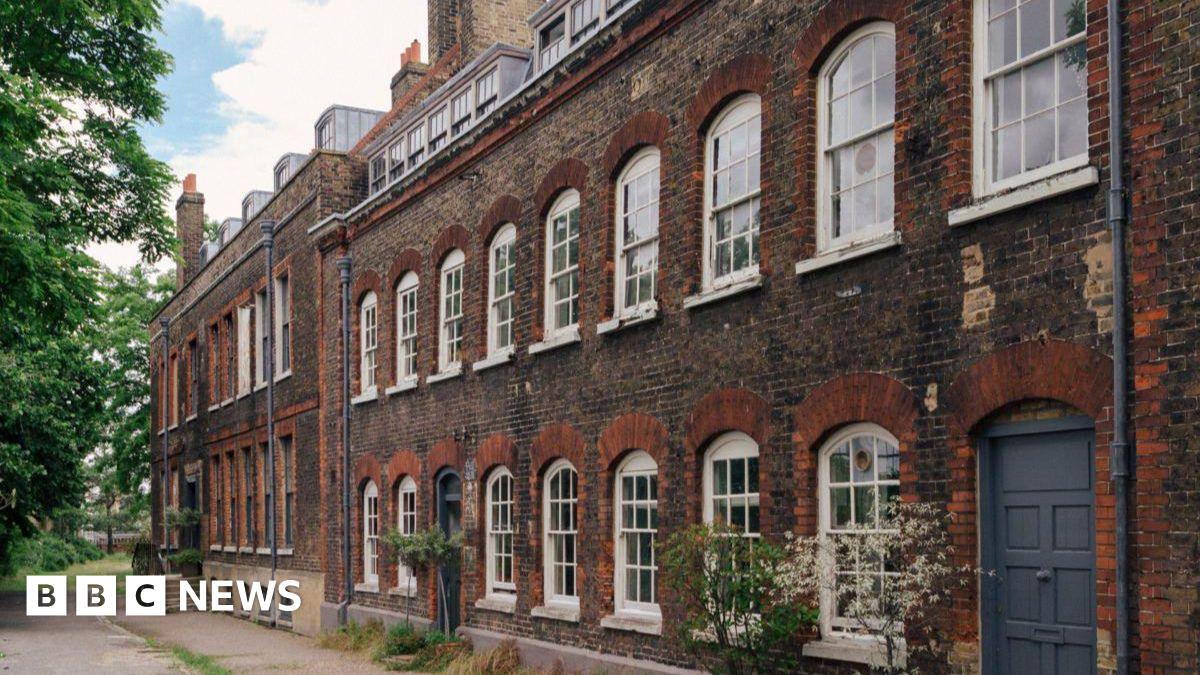 Exterior of brick building shows nine white sash windows upstairs and another seven downstairs plus a grey front door