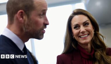The Prince and Princess of Wales laughing in a side view. Catherine, wearing burgundy, is in focus while William, wearing a suit, is blurry.