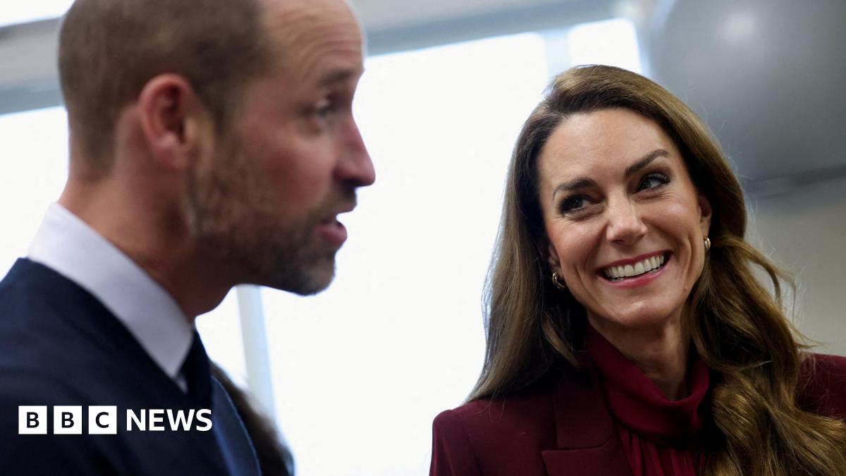 The Prince and Princess of Wales laughing in a side view. Catherine, wearing burgundy, is in focus while William, wearing a suit, is blurry.