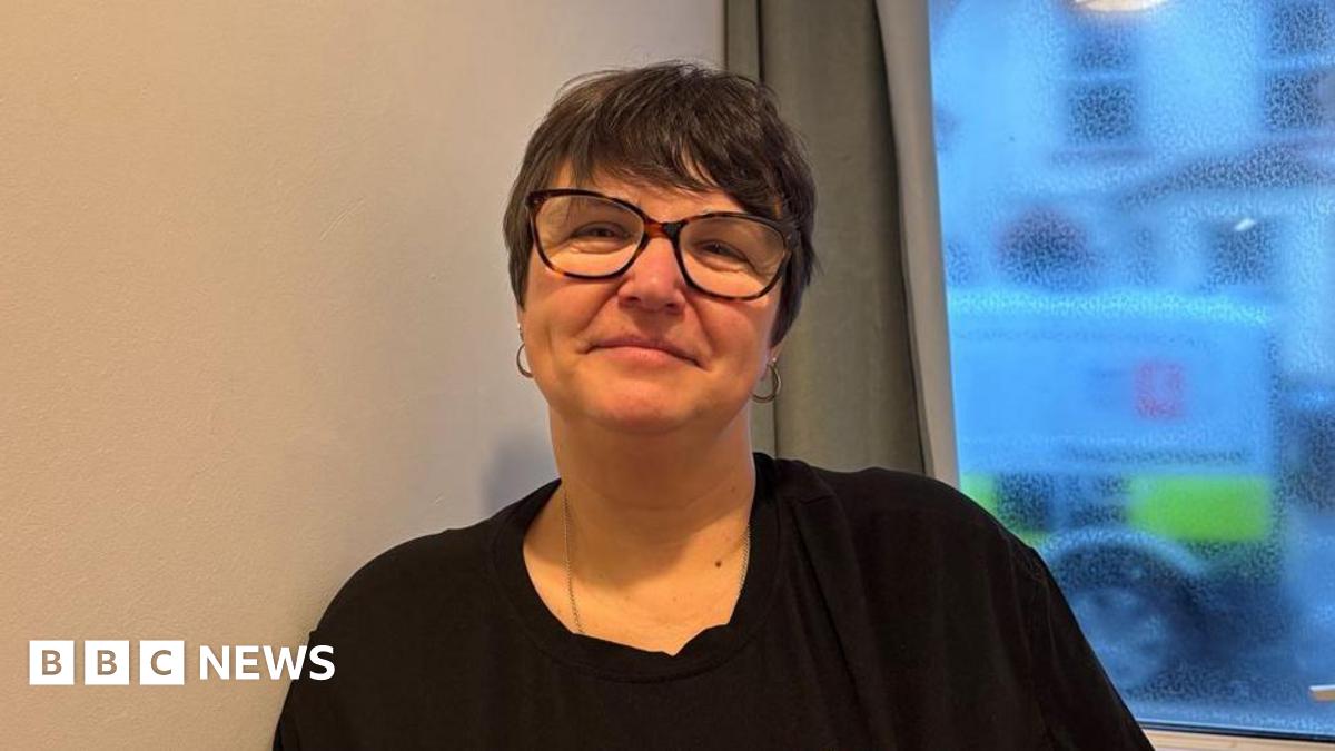 Michelle Grimes smiles looking directly into the camera. She has short brown hair and is wearing a black t-shirt, silver necklace, a pair of hooped earrings and tortoiseshell glasses.