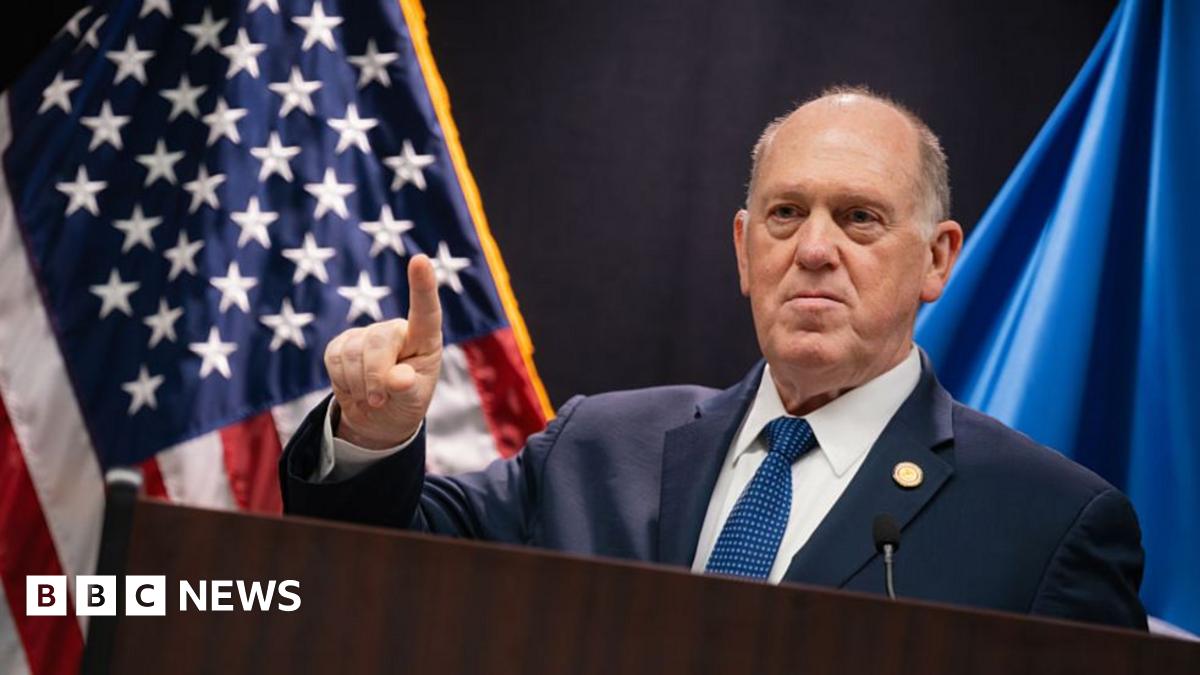 Frey in dark suit and black-and-white tie walks up stairs surrounded by reporters holding their phones out to record him