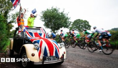 Fans wave flags in a car draped in a union jack as riders go past