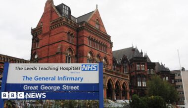 The exterior of Leeds General Infirmary, as indicated by an entrance sign indicating the reception is ahead. The hospital building itself is a grand old Victorian structure.