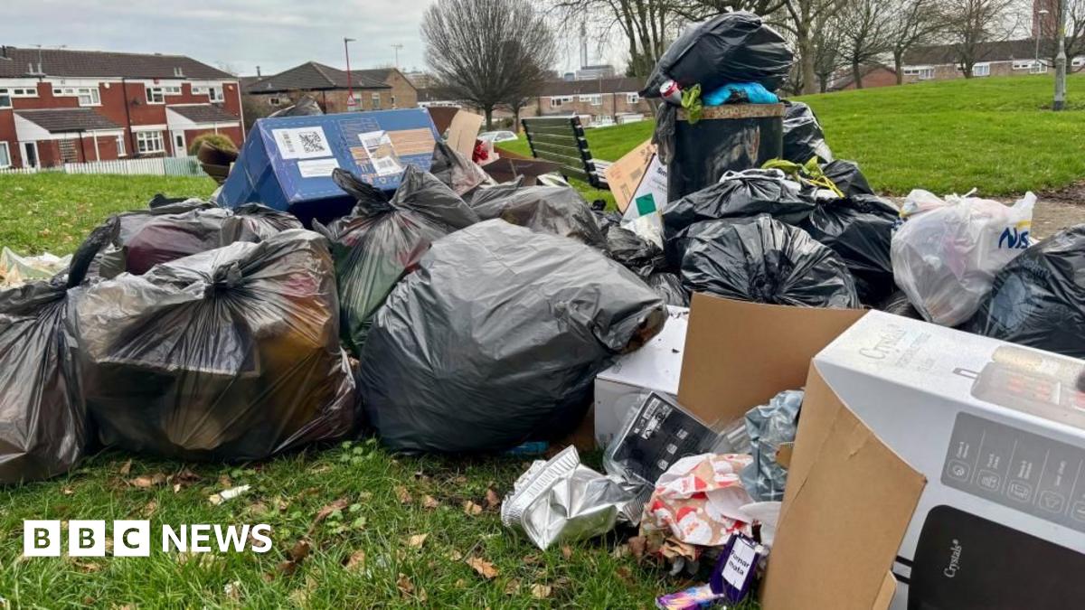 Lots of overflowing and split black rubbish bags and cardboard boxes left on a field
