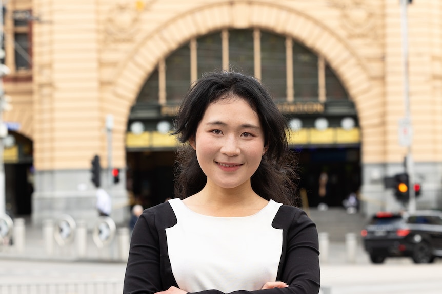 Angel Zhong poses with arms crossed in front of Flinders Street Station.