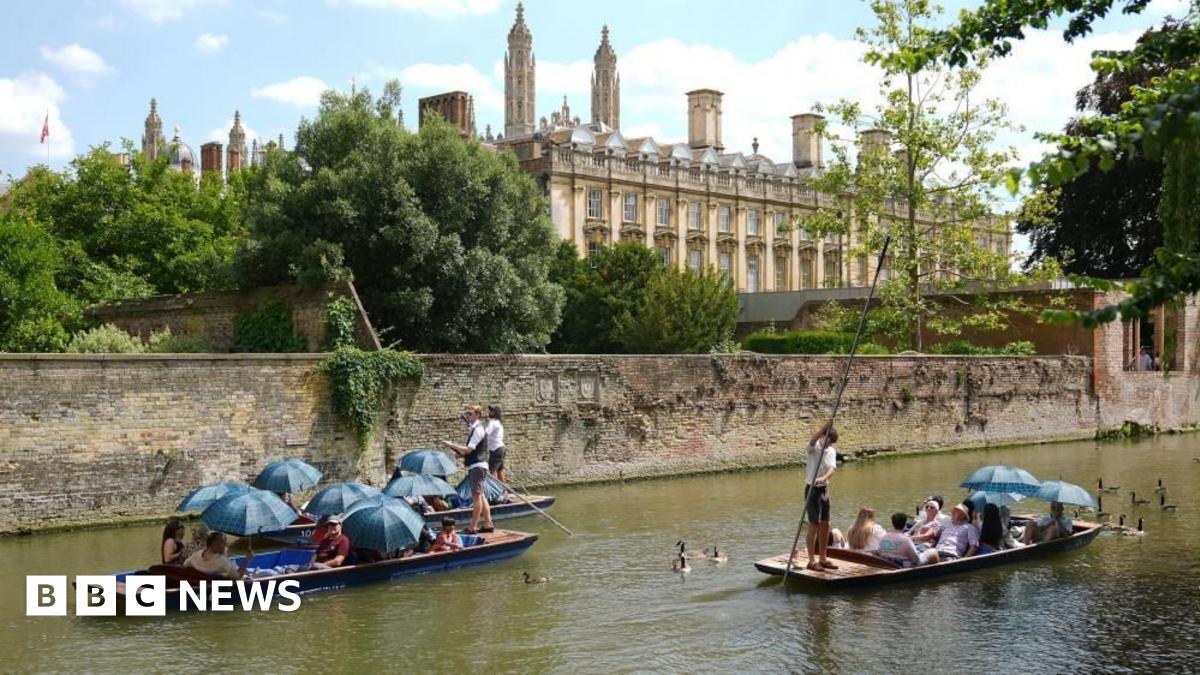 Punting in Cambridge. Three punts can be seen next to a walled section of the river. A university college building is in the background, and the spires or King's College Chapel.