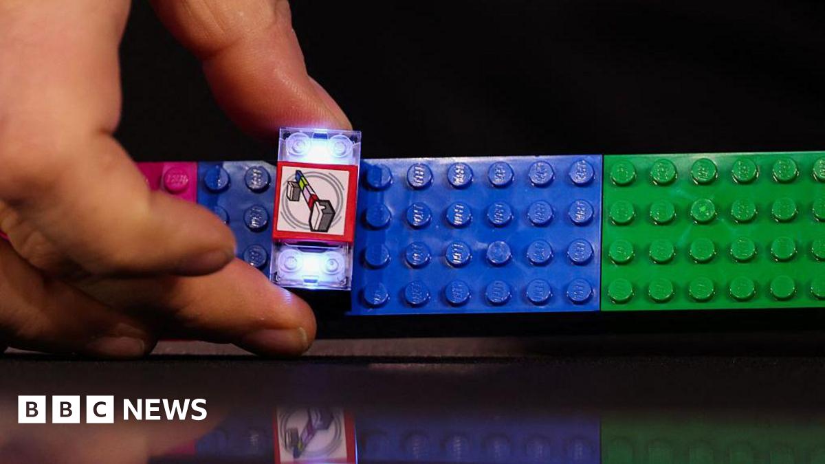 A close-up of a hand constructing a lit-up Lego Smart Brick on a set of pink, blue and green Lego blocks.