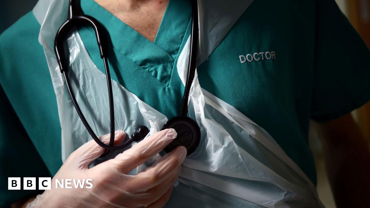 A picture of a doctor. He is wearing a green shirt and is wearing see-through gloves.
