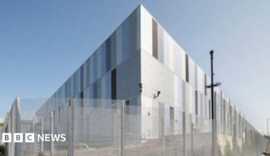 A large silver data centre building, with a mesh fence surrounding it.