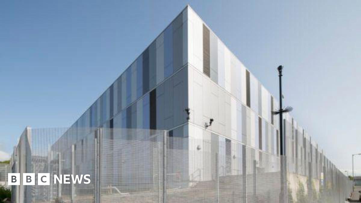 A large silver data centre building, with a mesh fence surrounding it.