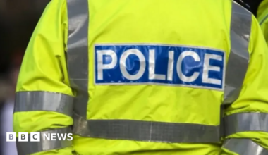 Getty image of the back of a police officer with a florescent yellow jacket that has POLICE in white letters with a blue box around it.