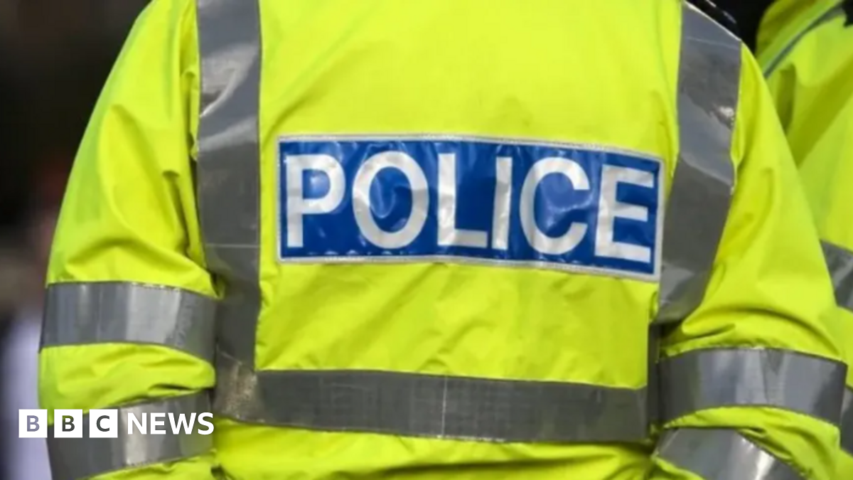 Getty image of the back of a police officer with a florescent yellow jacket that has POLICE in white letters with a blue box around it.