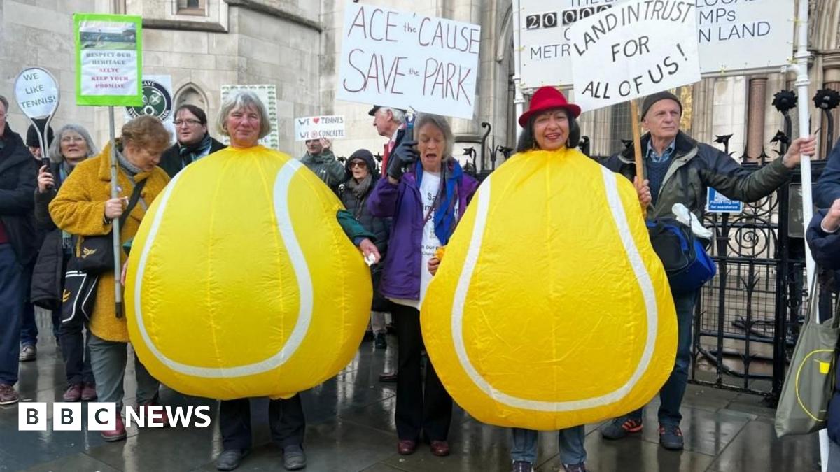 Two women dressed as tennis balls protest outside Royal Courts of Justice with other members of Save Wimbledon Park. They hold various signs with writing such as "Land In Trust For All Of Us!".