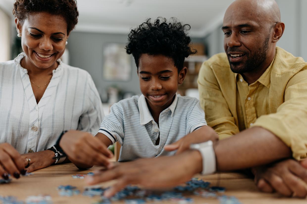 A family, consisting of parents and two kids, is joyfully engaged in completing a jigsaw puzzle at a wooden table, showcasing a moment of unity, fun, and shared effort in their home.