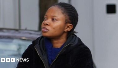 A woman wearing a blue dress and a black jacket has her arms folded as she is walking by the steps to the court.