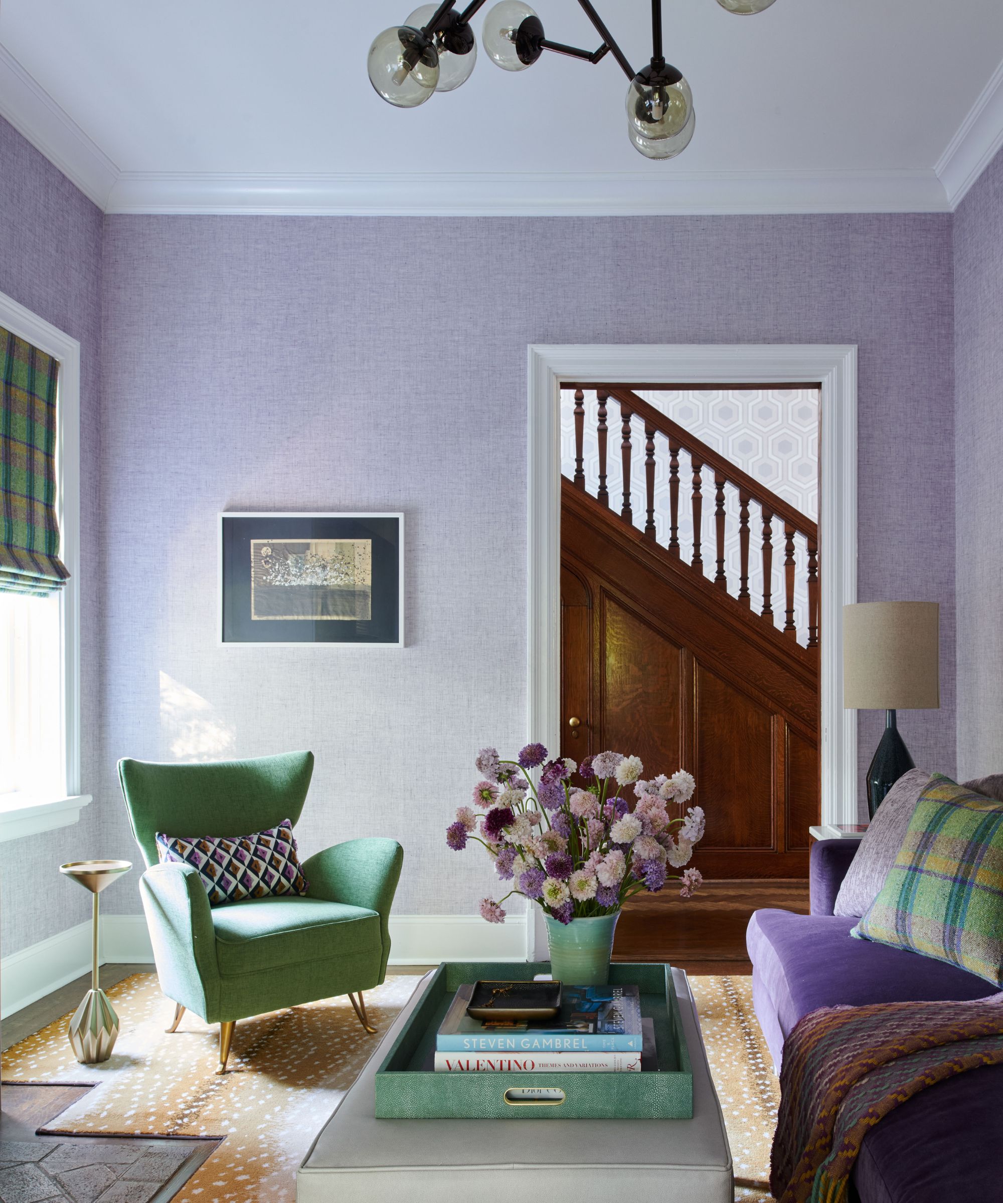 A living room with lilac walls, a green armchair, and a coffee table with a green tray and a vase of lilac flowers.