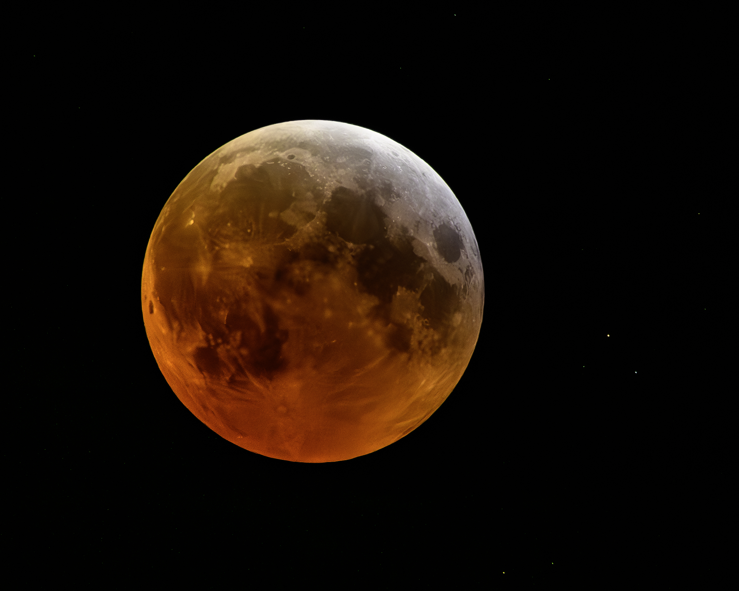 Close up image showing a full moon tinted reddish orange against a black background.