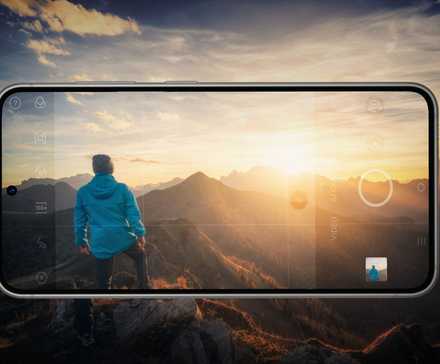 A smartphone captures a person on a mountain at sunset, blending reality with digital photography.