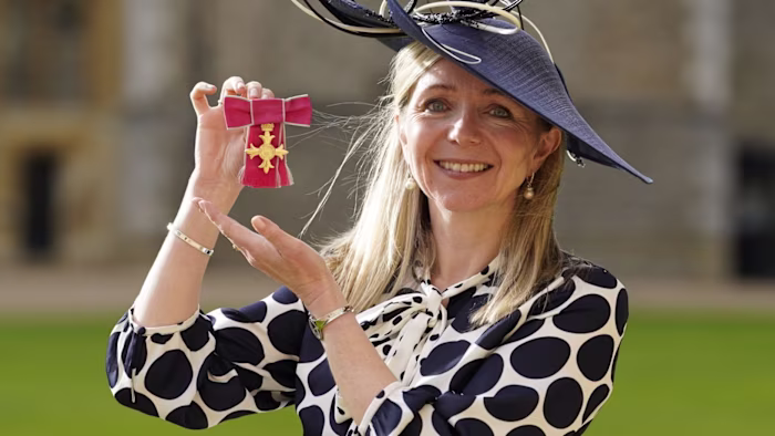 Dr Melanie Ivarsson smiles and holds up her OBE medal after an investiture ceremony at Windsor Castle.