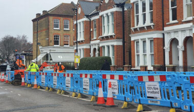 Workers in high-visibility clothing install fibre optic broadband behind blue barriers on a residential street in Clapham, London.