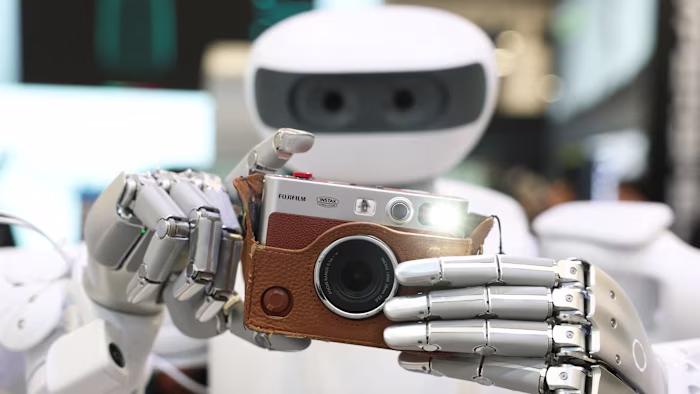 The Sharpa robot holds a Fujifilm instax camera and takes a photo, with the camera flash illuminated, at CES 2026.