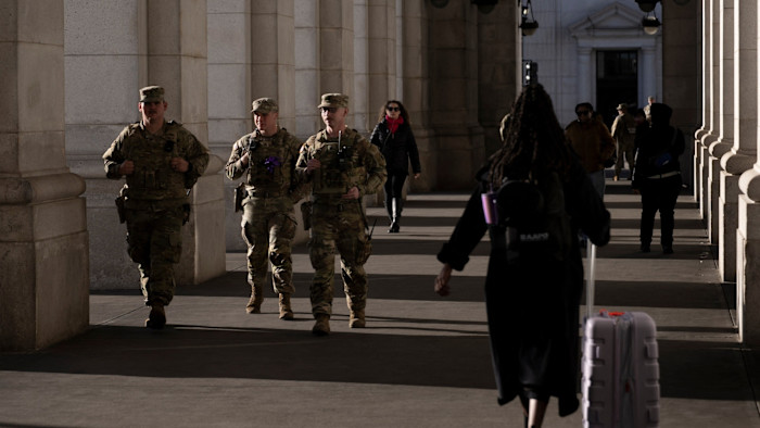 Three National Guard members in uniform walk past travelers in a colonnade at Union Station.