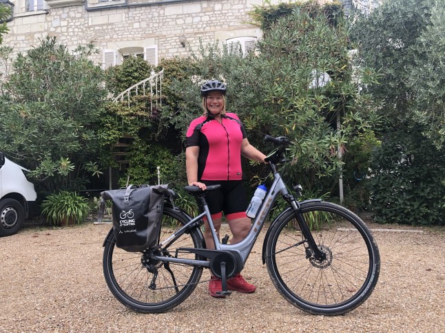 Jenny Forsyth in a pink top and black shorts, standing with an e-bike in front of a green area.