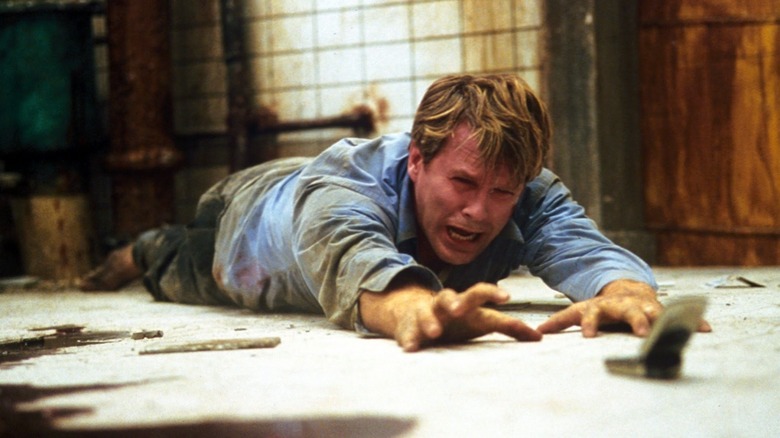 Cary Elwes as Dr. Gordon on the floor reaching for a cell phone while crying in Saw