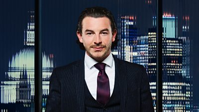 A man with slicked back hair and a pinstripe suit smiles in front of a city backdrop at night
