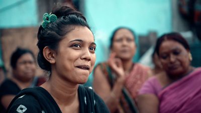 Close-up of a woman smiling. Blurred in the background are other women sat nearby. 